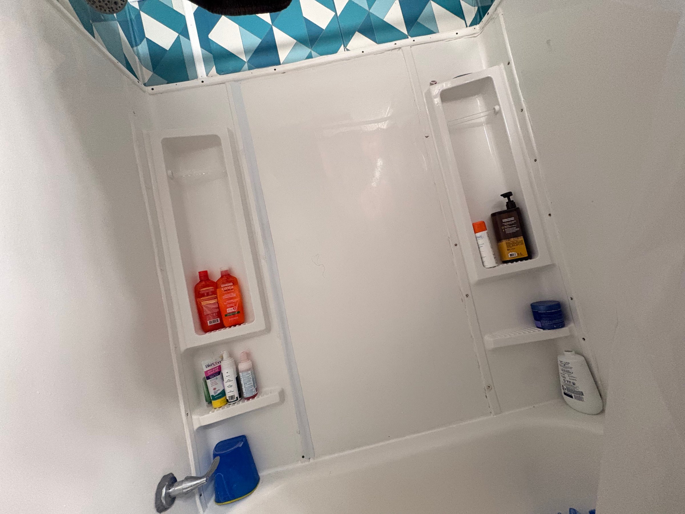 Original white tub surround with blue geometric wall finish before renovation