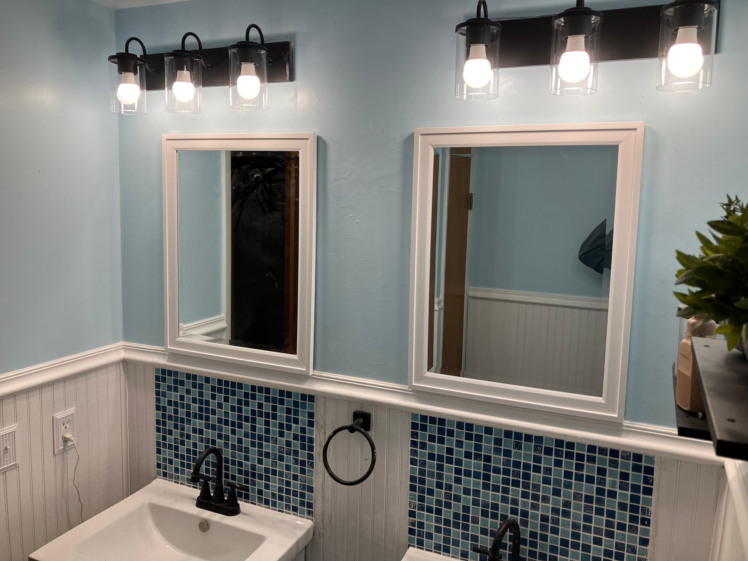 Finished blue bathroom with white trim, mirrors, lighting, and mosaic backsplash