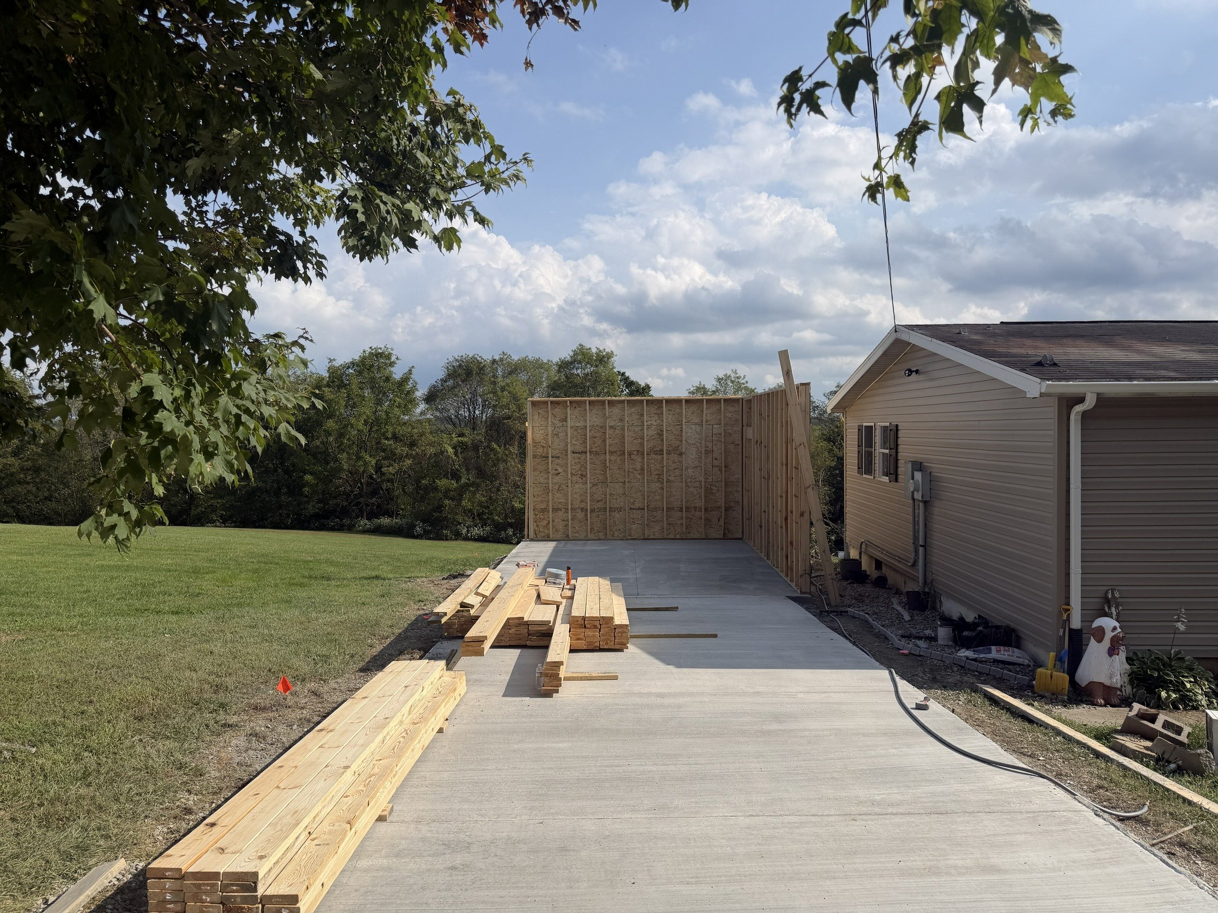 Concrete slab and wall framing beside a home, with materials staged for ongoing work